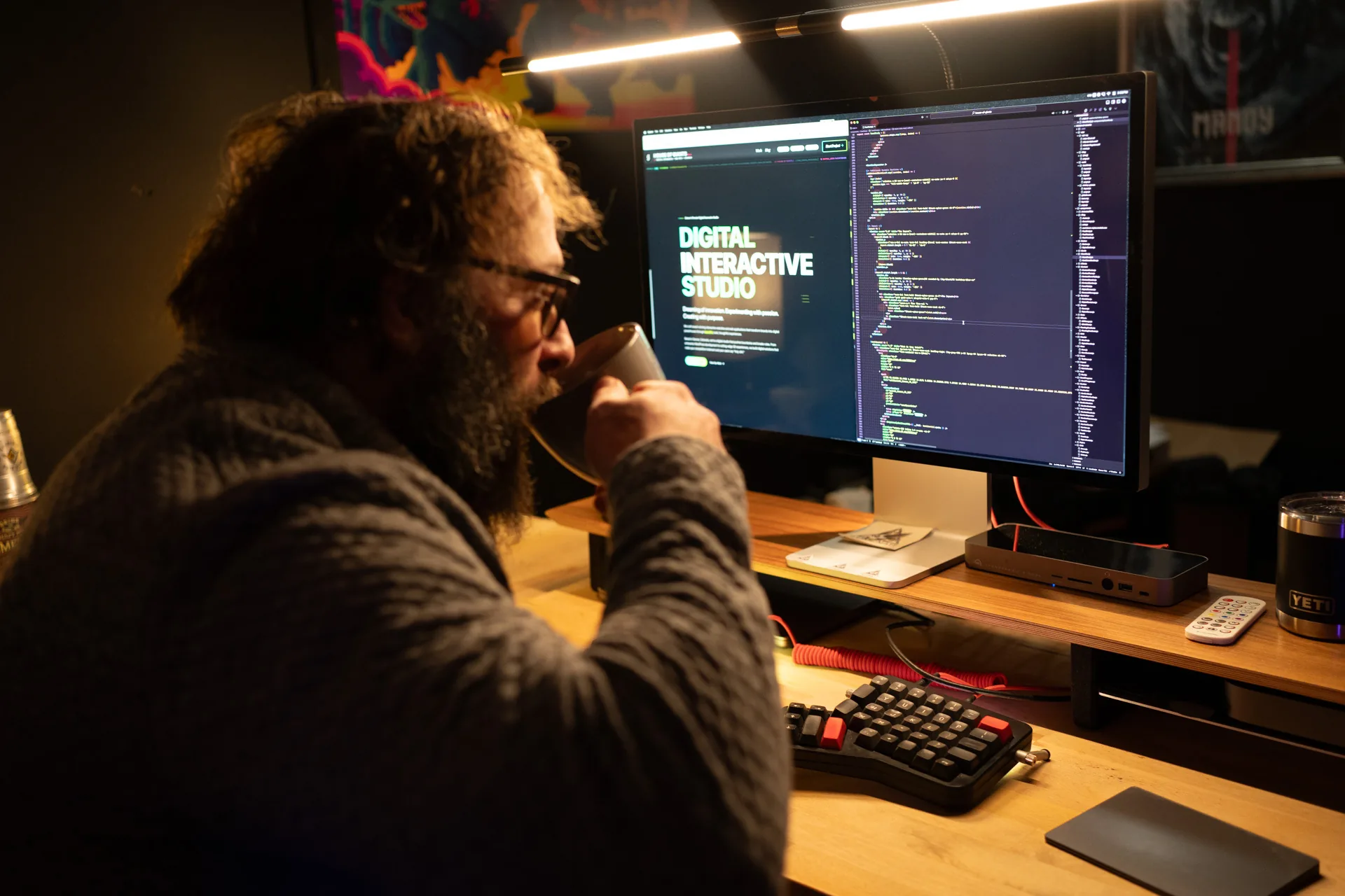 Dom at his desk with a coffee, code on the monitor in front of him.